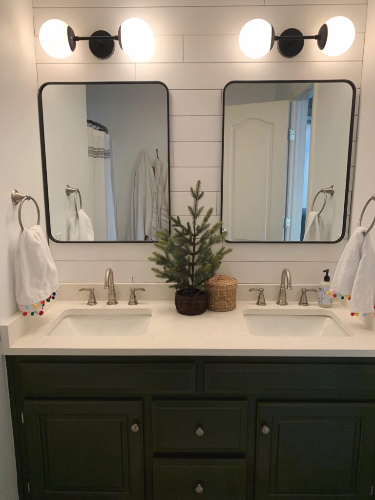 dark green bathroom vanity with shiplap wall and black mirrors.