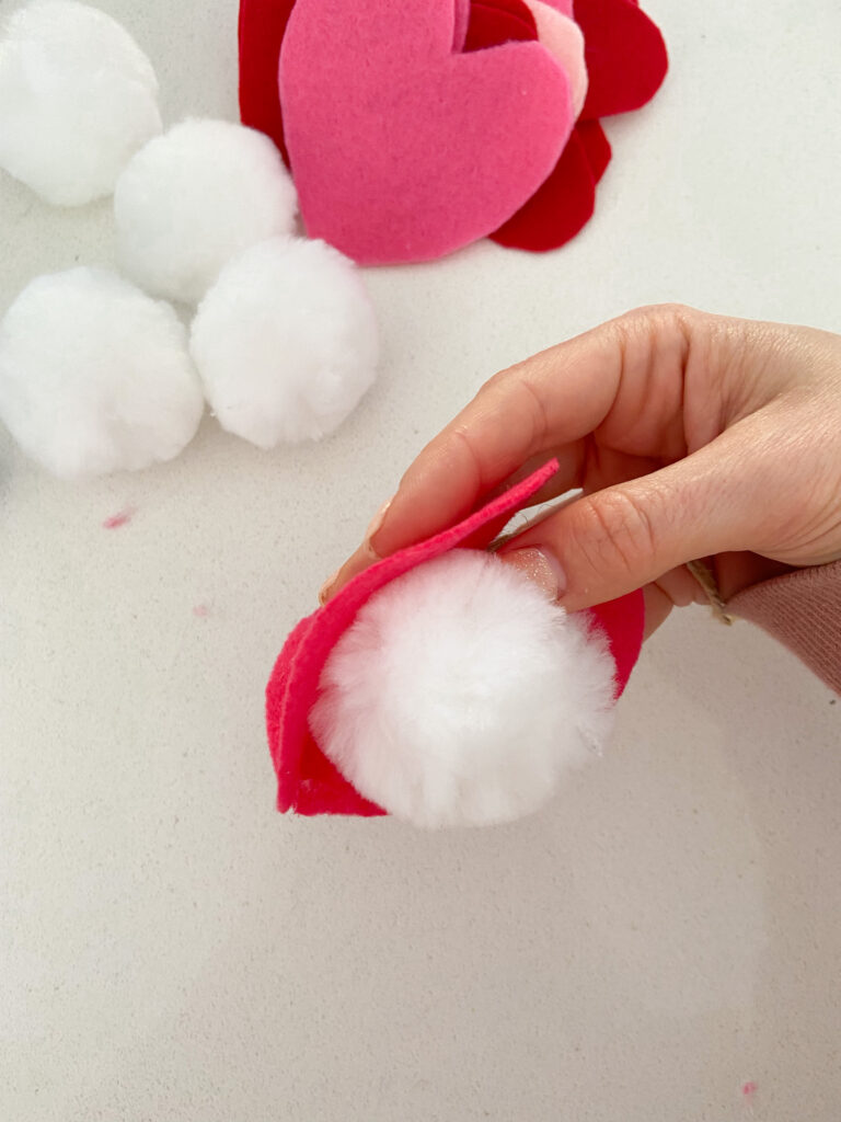 Pom pom being added to felt heart shapes that have been glued together. 
