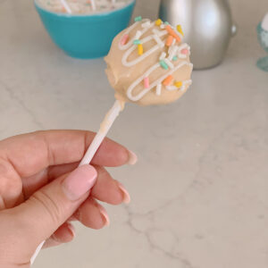 Hand holding pastel cake pop with sprinkles.