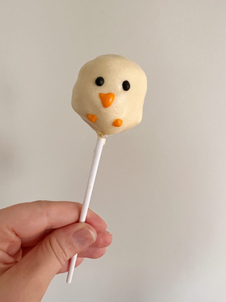 yellow cake pop with beak and eyes being held.