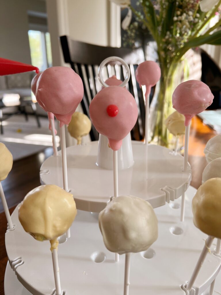 royal icing being used to decorate pink cake pop.