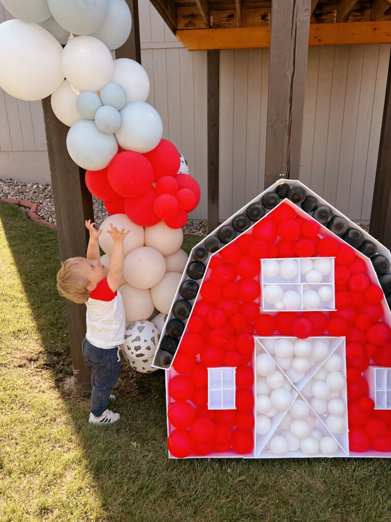 toddler reaching for balloon arch and playing by barn balloon mosaic.