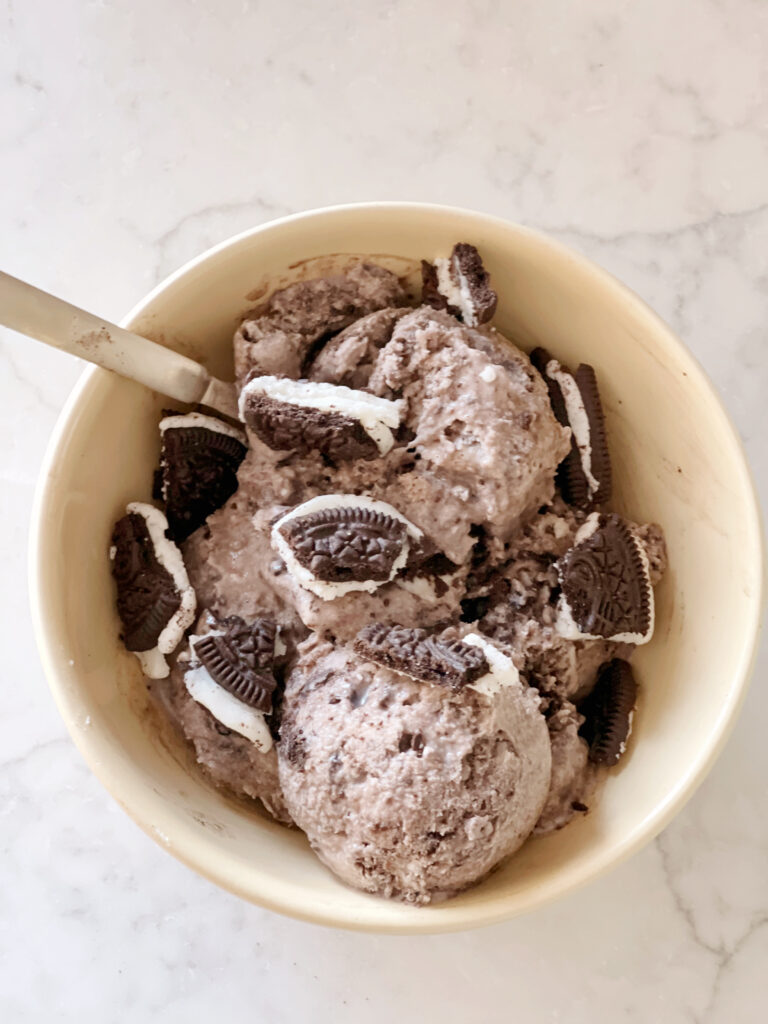 ice cream with oreo cookie toppings in a yellow bowl with spoon.