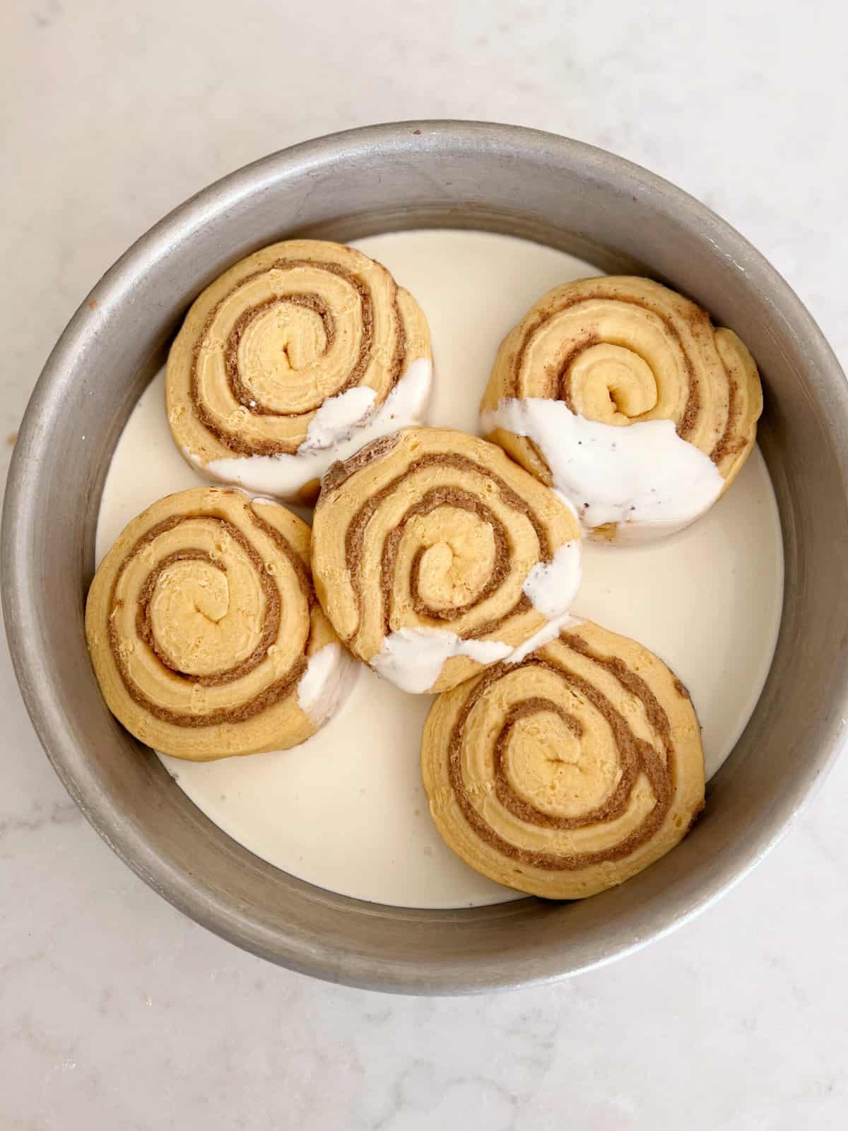 cinnamon rolls sitting in heavy whipping cream in a baking dish