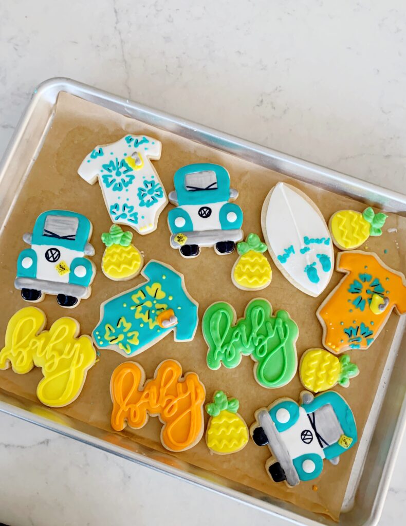Tropical themed baby shower cookies with a onesie, bus pineapples and surfboard. 