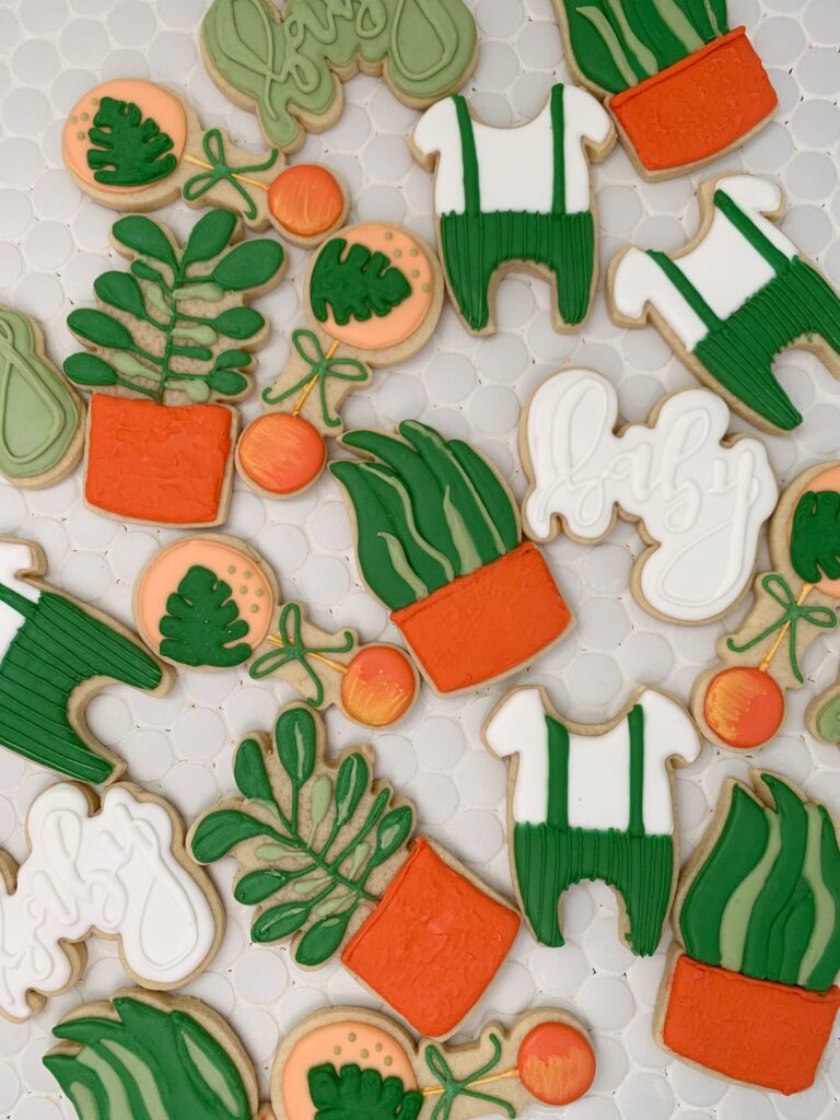 Cookies shaped into a baby outfit and to look like plants and succulents. 