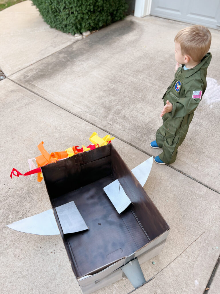 toddler standing by cardboard box plane in Top Gun Halloween costume. 