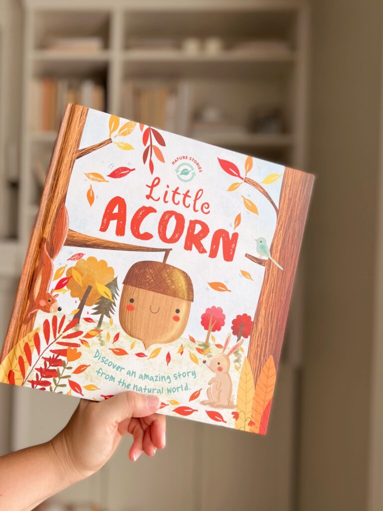 little acorn book being held in front of bookcase.