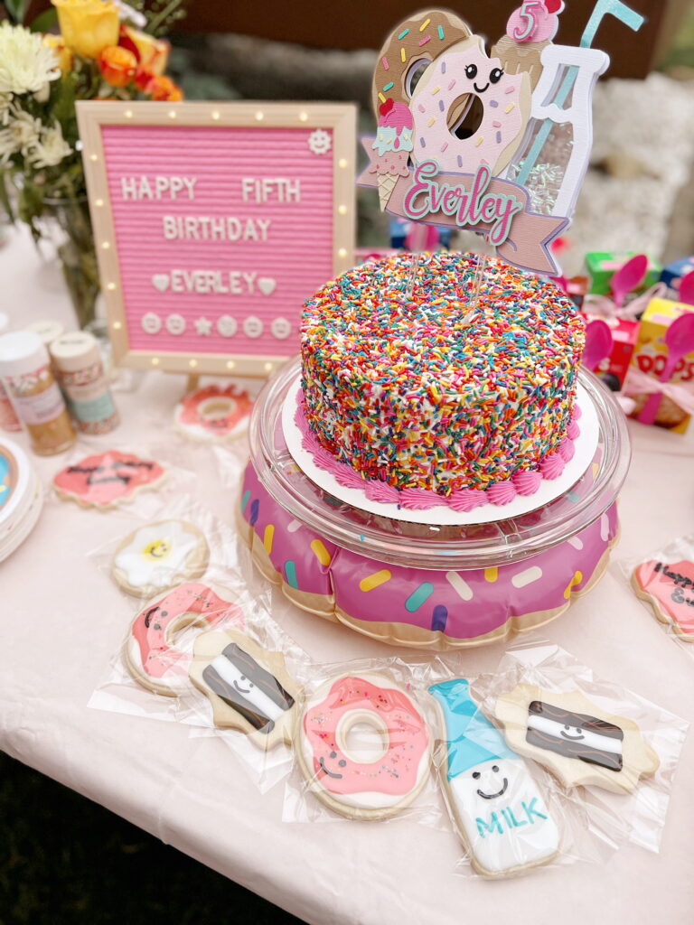 table with birthday cake and donut themed cake topper on it. 