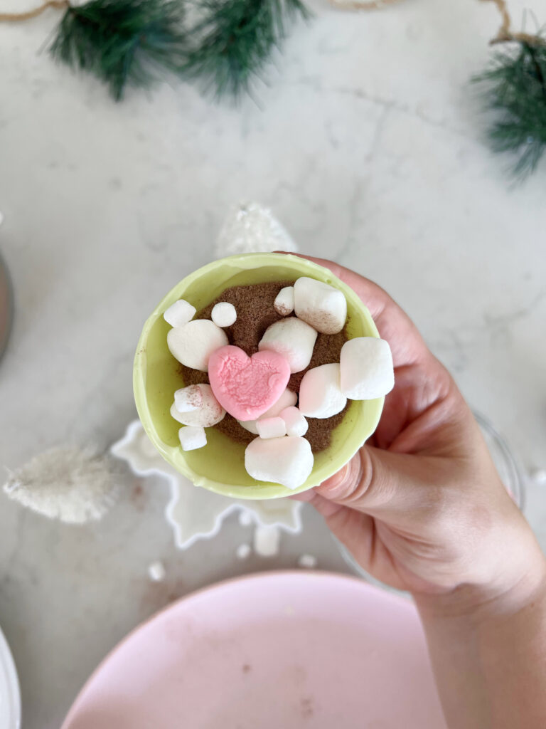 Hot cocoa bomb shell filled with hot cocoa mix and marshmallows, including a pink heart marshmallow. 