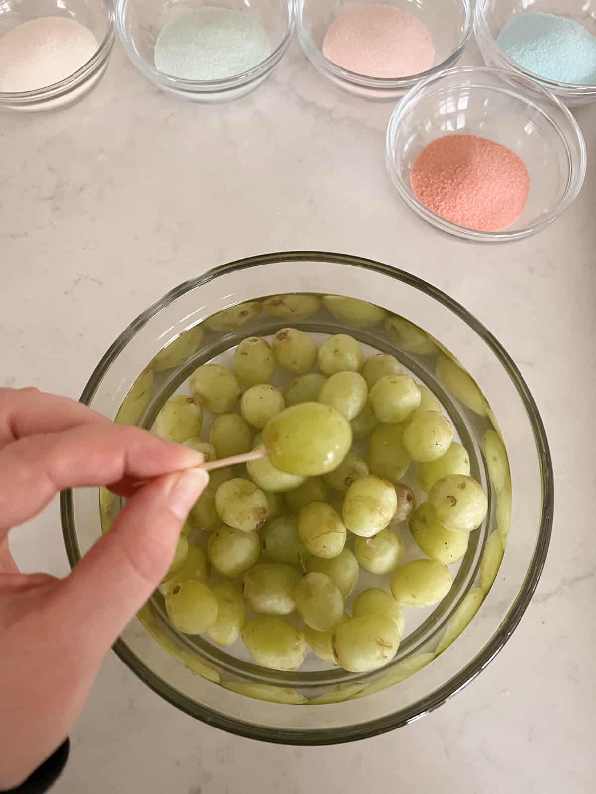 green grape on a toothpick over a bowl of green grapes in water. 