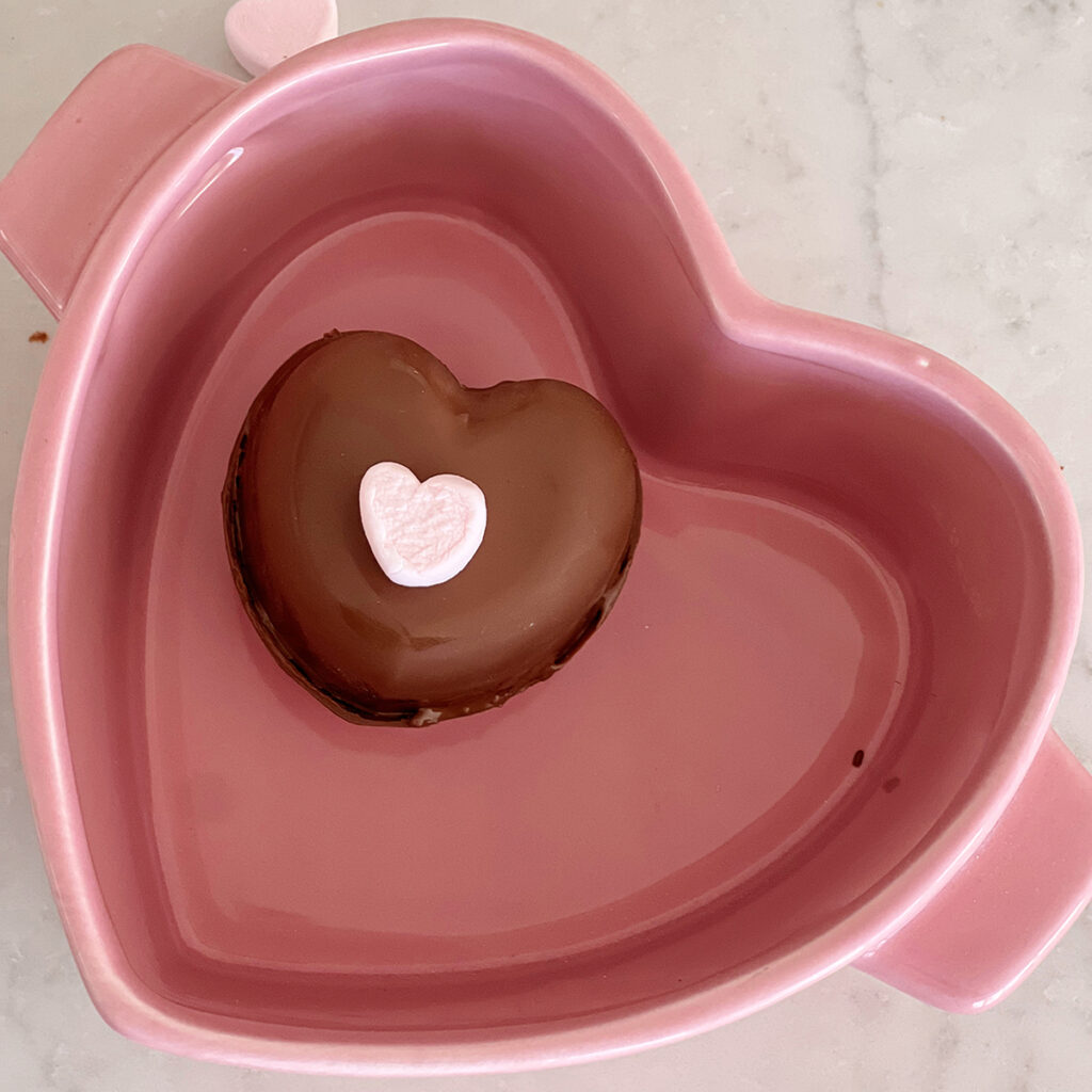 Heart-shaped hot cocoa bomb in a heart shaped baking dish. 