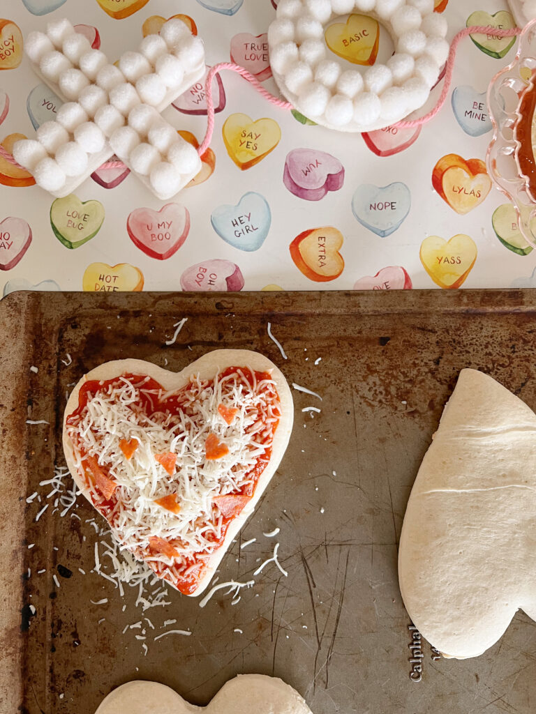 Heart-shaped pepperoni slices on pizza dough. 