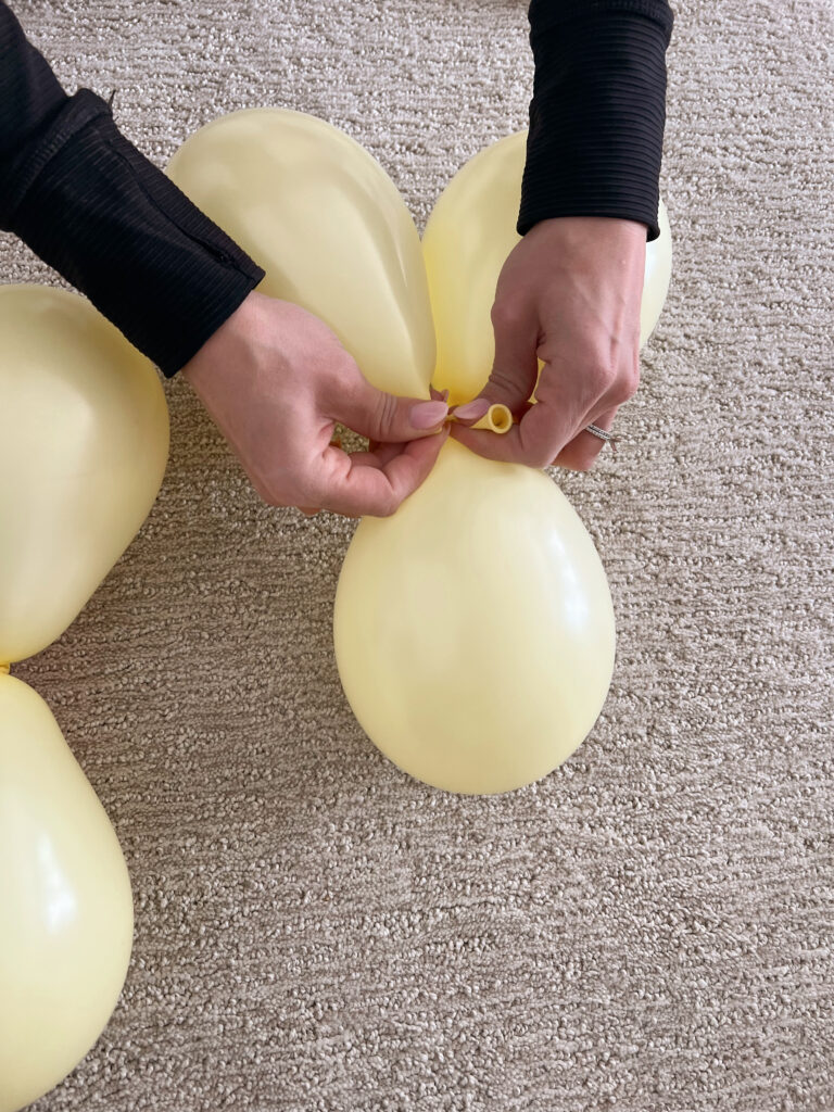 Tying a yellow balloon into a pair or grouping of balloons. 