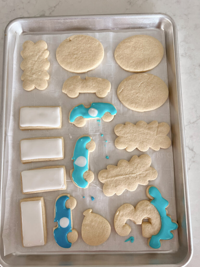 Car-shaped sugar cookies being decorated with blue and white royal icing. 