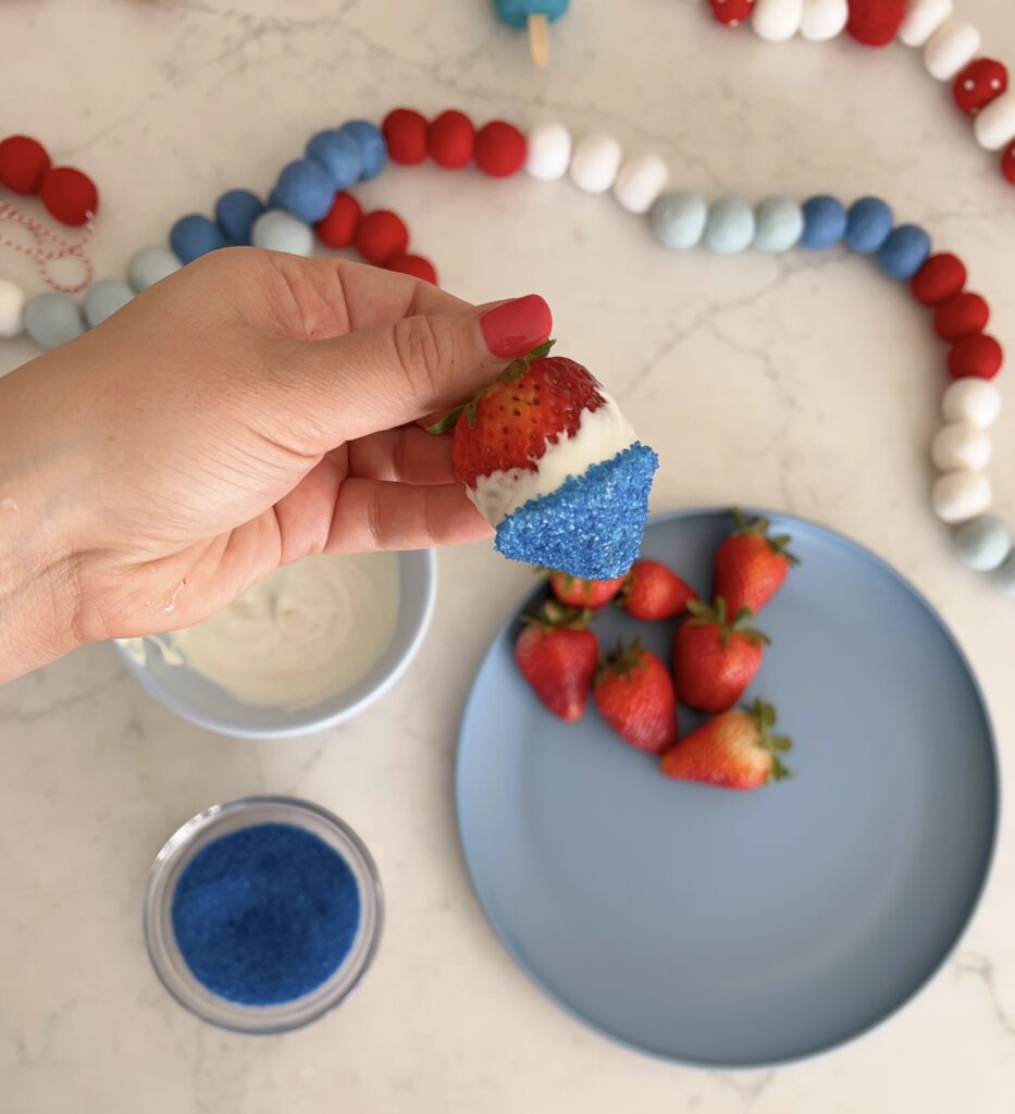 Strawberry being held that has been dipped into blue sprinkles. 