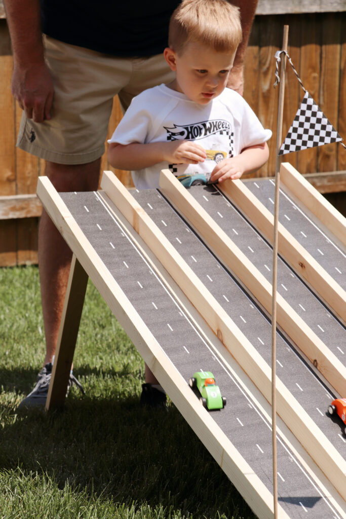 child running a car down a hot wheels race track ramp. 