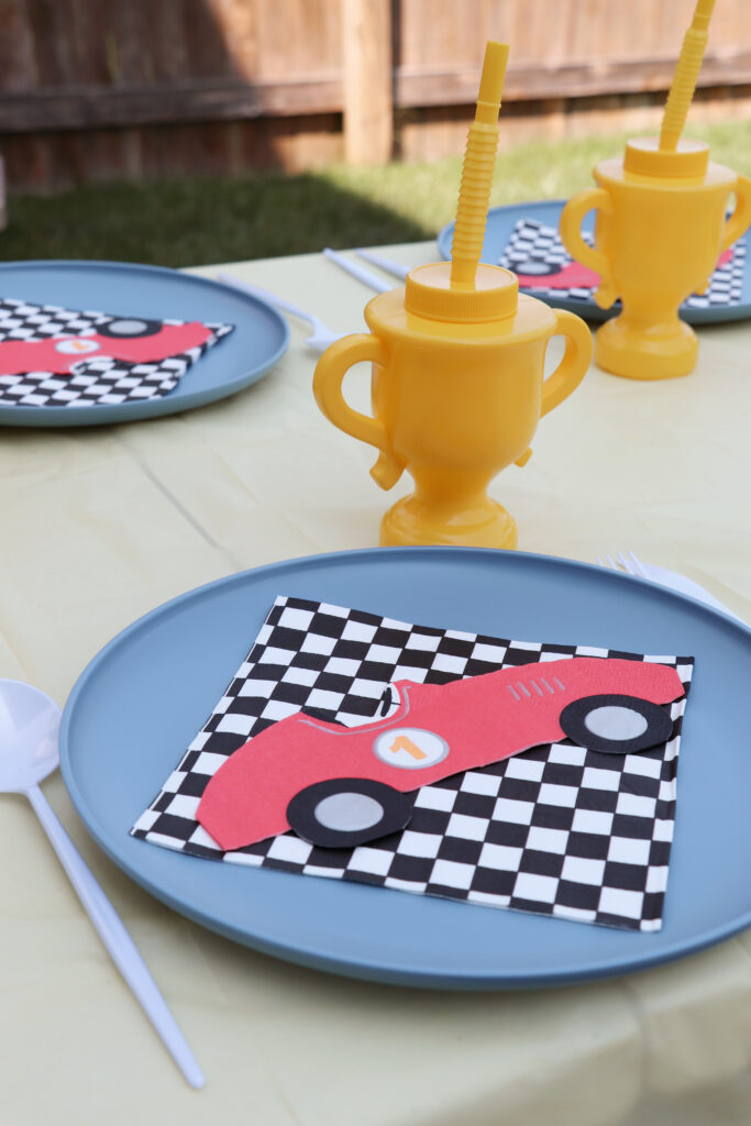 blue plastsic plate with checkered and car-shaped napkin on it next to a plastic yellow trophy cup. 