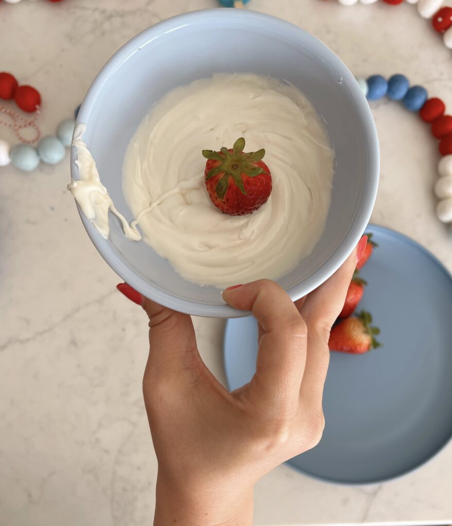 strawberry being dipped into bowl of melted white chocolate. 