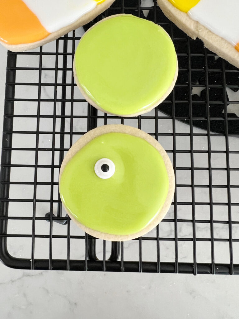 Circle shaped sugar cookie with green frosting being decorated as a monster for Halloween. 