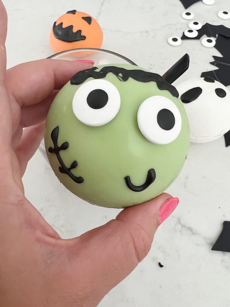 Googley eyes added to a green hot cocoa bomb with black icing for details of face. 