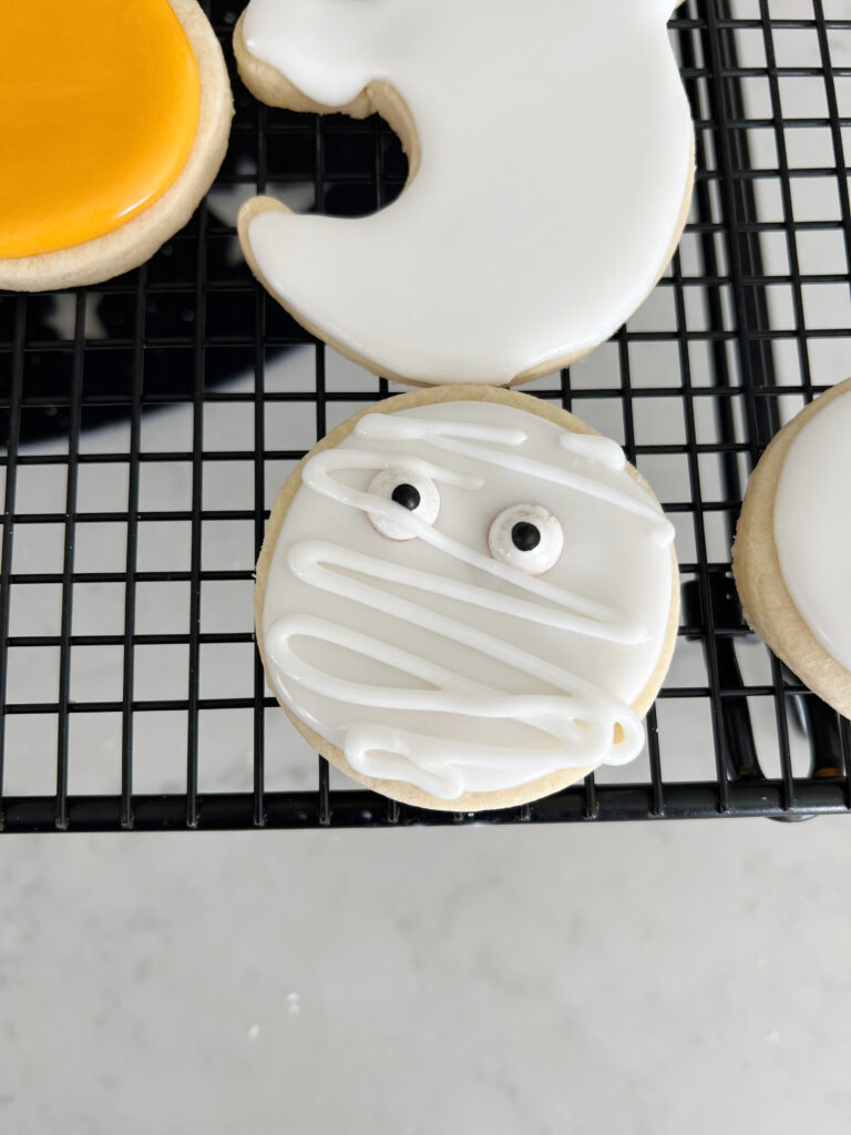Sugar cookie decorated with googley eyes and white royal icing to look like a mummy. 