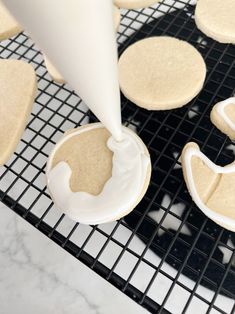 Circle sugar cookie being filled with white icing. 