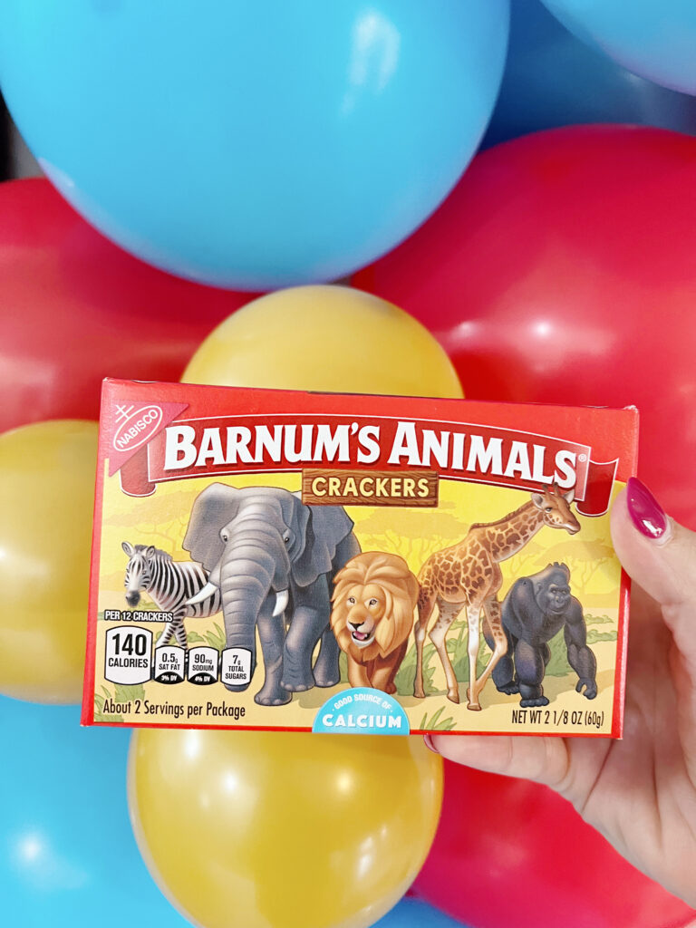 Animal crackers held in front of gold, blue and red balloons. 