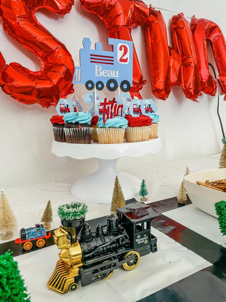 Train themed birthday party with cupcakes and decorations including a toy train. 