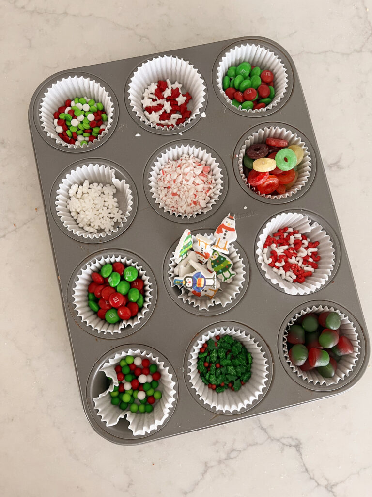 Muffin tin filled with sprinkles and candies in liners. 